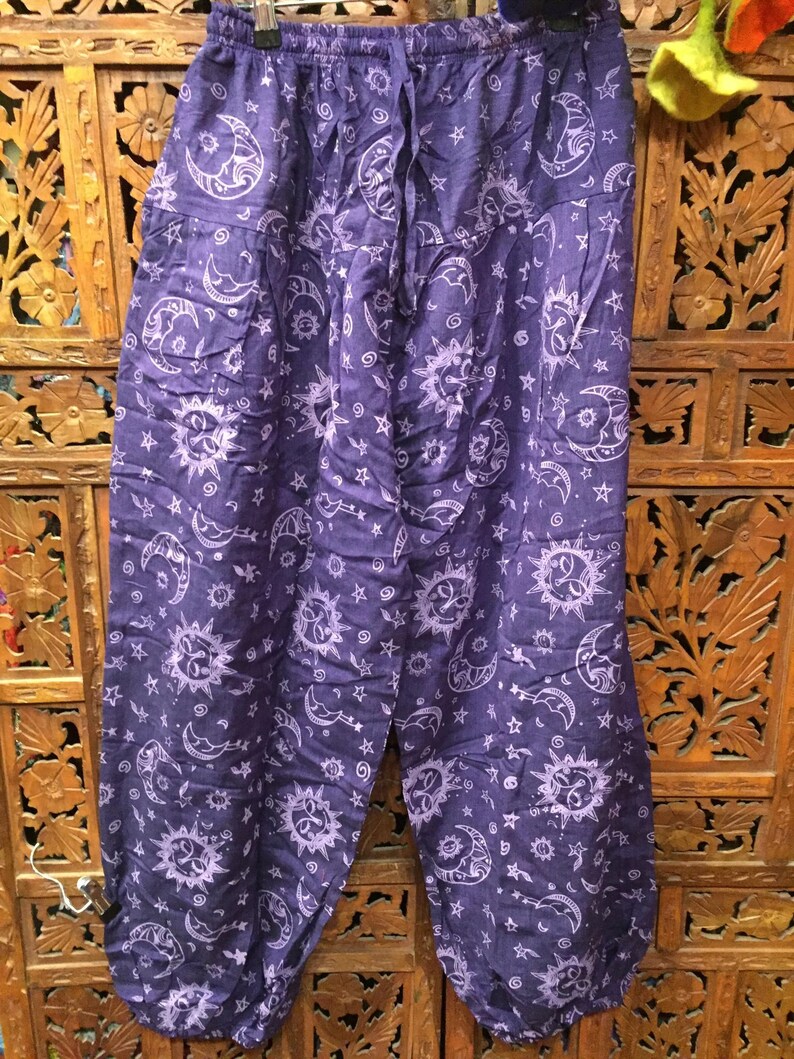 May include: Purple cotton pants with a white sun and moon print. The pants have an elastic waistband and a drawstring.