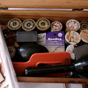 May include: A wooden sewing box filled with various supplies including multiple wooden spools of J.P. Coats thread, a package of needles labeled Needles Embroidery 12 Needles SIZE 1/5, a red plastic tool, a black darning egg, and other sewing notions.