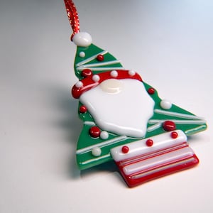 May include: A Christmas tree ornament in the shape of Santa Claus. The ornament is green with red and white accents, including a red hat and white beard. It has a red and white striped base and a red ribbon for hanging.