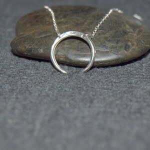 May include: A silver crescent moon necklace on a chain, resting on a gray stone.