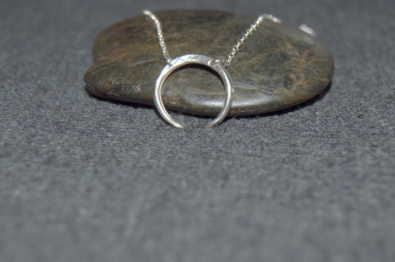 May include: A silver crescent moon necklace on a chain, resting on a gray stone.
