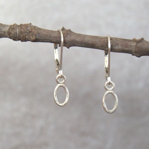 May include: A pair of silver hoop earrings with a small oval charm hanging from each hoop.