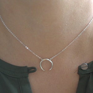 May include: A silver necklace with a crescent moon pendant. The necklace is on a model wearing a green shirt.
