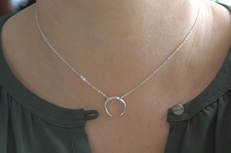May include: A silver necklace with a crescent moon pendant. The necklace is on a model wearing a green shirt.