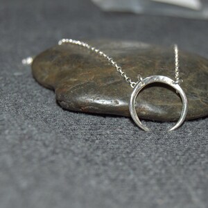 May include: A silver crescent moon pendant necklace on a silver chain, resting on a gray rock.