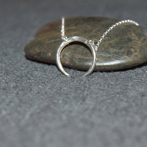 May include: A silver crescent moon necklace on a gray stone background.