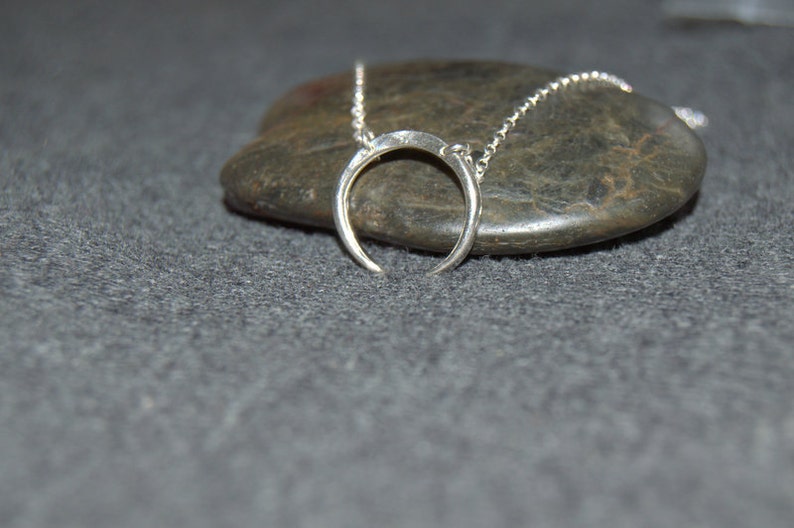 May include: A silver crescent moon necklace on a gray stone background.