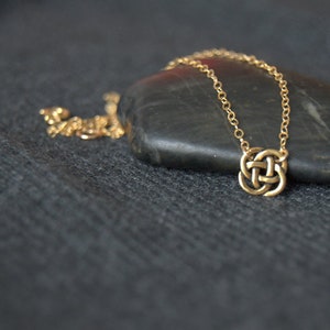 May include: A gold chain necklace with a Celtic knot pendant. The necklace is lying on a dark gray surface.
