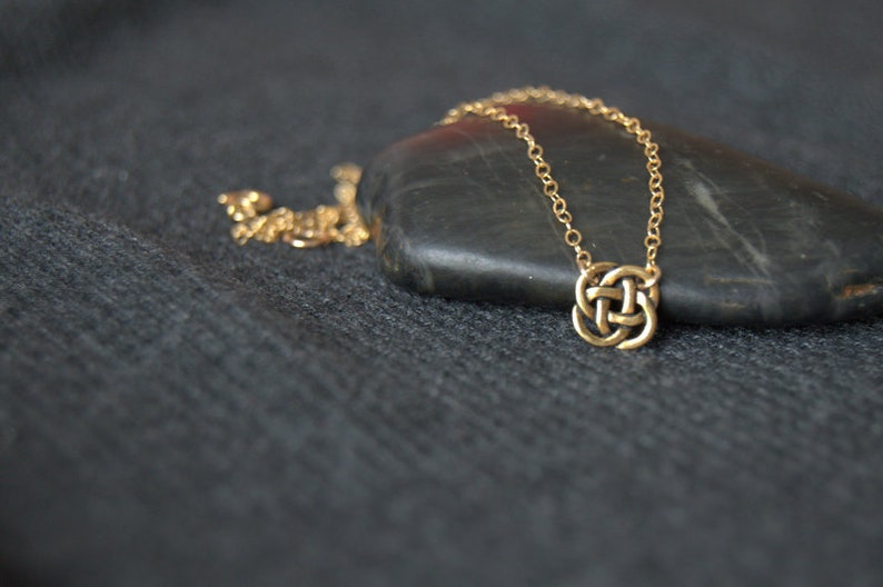 May include: A gold chain necklace with a Celtic knot pendant. The necklace is lying on a dark gray surface.