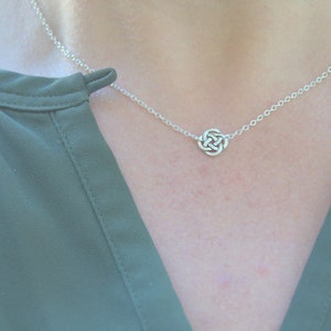 May include: A silver chain necklace with a small, intricate knot pendant.