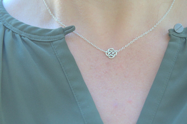 May include: A silver chain necklace with a small, intricate knot pendant.