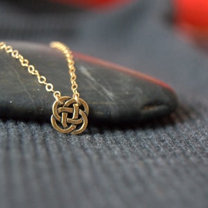 May include: A gold chain necklace with a Celtic knot pendant. The pendant is a circular design with intricate knotwork.