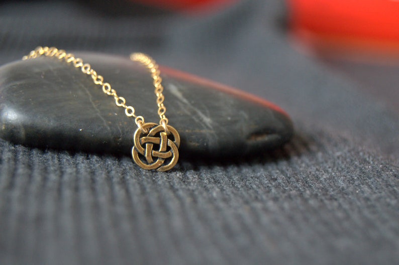 May include: A gold chain necklace with a Celtic knot pendant. The pendant is a circular design with intricate knotwork.