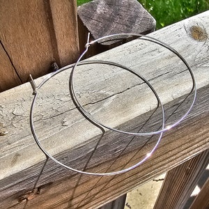 May include: Two silver hoop earrings on a wooden surface. The hoops are thin and delicate, and they are stacked on top of each other.