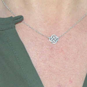 May include: A silver chain necklace with a Celtic knot pendant. The necklace is on a person's chest.