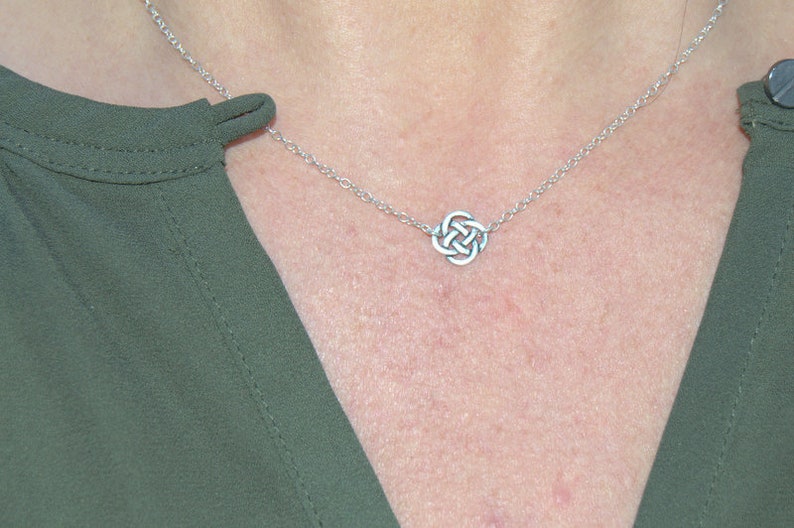 May include: A silver chain necklace with a Celtic knot pendant. The necklace is on a person's chest.