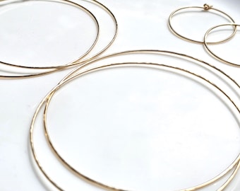 May include: A collection of gold hoop earrings in varying sizes. The set includes two large, thin, smooth gold hoops and two smaller, delicate gold hoops. Each earring features a simple circular wire design with a small clasp closure mechanism.