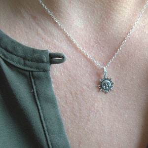 May include: A silver chain necklace with a small sun pendant. The sun has a face and is detailed with rays.
