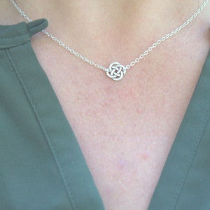 May include: A silver chain necklace with a small, intricate Celtic knot pendant. The necklace is worn by a person wearing a green shirt.