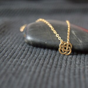 May include: A gold chain necklace with a Celtic knot pendant. The necklace is displayed on a dark gray surface.