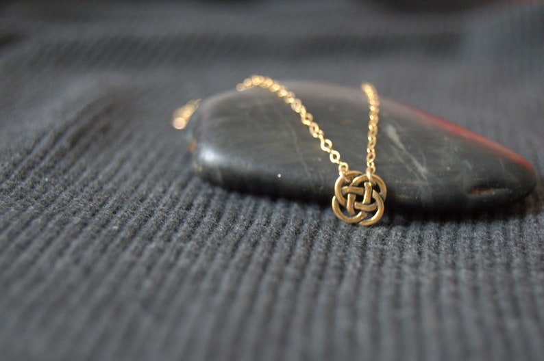 May include: A gold chain necklace with a Celtic knot pendant. The necklace is displayed on a dark gray surface.