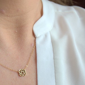 May include: A gold chain necklace with a small, intricate knot pendant.
