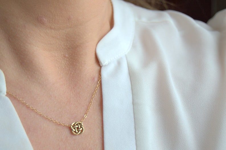 May include: A gold chain necklace with a small, intricate knot pendant.