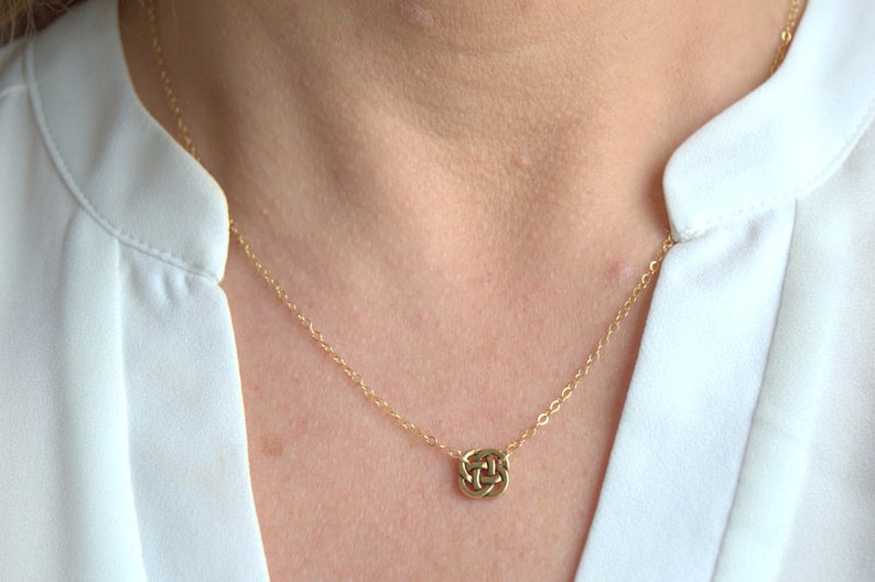 May include: A gold chain necklace with a small, intricate knot pendant.