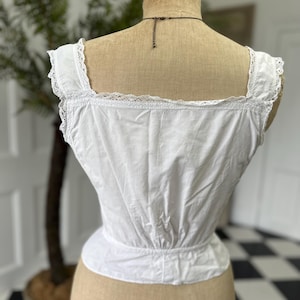 Puede incluir: Camis&oacute;n de algod&oacute;n blanco con ribete de encaje. El camis&oacute;n tiene una cintura fruncida y es sin mangas.