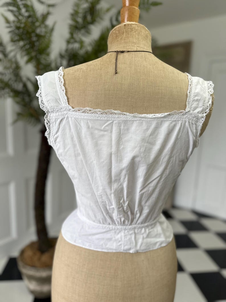 Puede incluir: Camis&oacute;n de algod&oacute;n blanco con ribete de encaje. El camis&oacute;n tiene una cintura fruncida y es sin mangas.