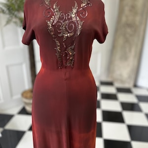 Peut inclure: Une longue robe bordeaux avec un motif de paillettes sur le corsage. La robe a un effet ombré, passant à une teinte rouge plus claire en bas.