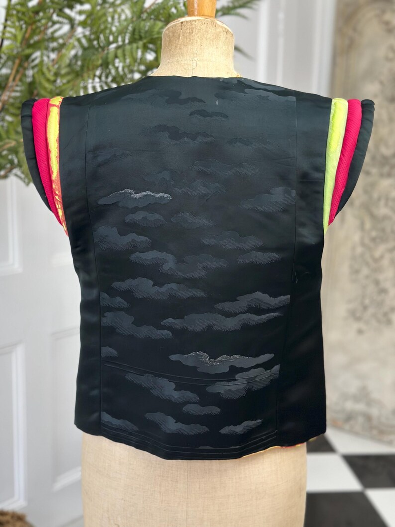 Puede incluir: Chaleco negro sin mangas con un patr&oacute;n de nubes y ribete de colores. El ribete es una combinaci&oacute;n de rosa, amarillo y verde.