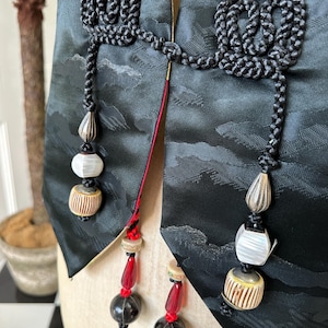 Puede incluir: Un chaleco de seda negro con intrincados detalles de cord&oacute;n negro y cuentas decorativas. El chaleco tiene un ribete rojo y dorado y presenta un dise&ntilde;o &uacute;nico con un patr&oacute;n de nubes.
