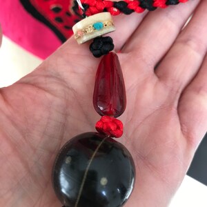 Puede incluir: Un collar de cuentas negras y rojas con una gran cuenta negra redonda, una cuenta roja m&aacute;s peque&ntilde;a y una cuenta blanca con acentos turquesa.