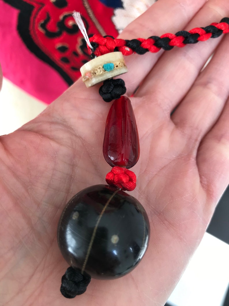Puede incluir: Un collar de cuentas negras y rojas con una gran cuenta negra redonda, una cuenta roja m&aacute;s peque&ntilde;a y una cuenta blanca con acentos turquesa.