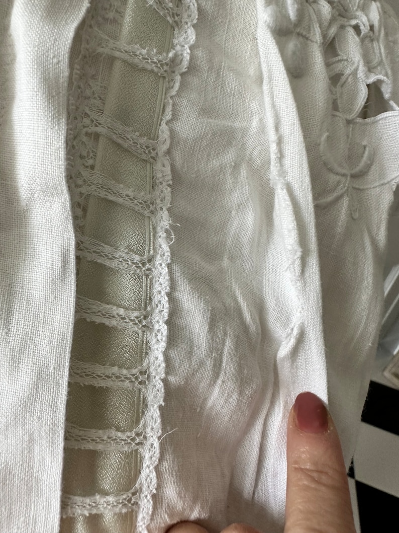 May include: White linen fabric with a delicate lace trim. The fabric has a slightly textured surface and is folded over on itself.