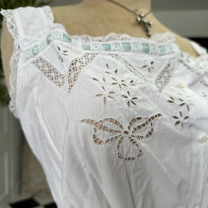 Puede incluir: Top blanco de algod&oacute;n con delicado encaje y dise&ntilde;os de corte intrincados. El top presenta un motivo de mariposa y una fila de botones peque&ntilde;os en la parte delantera.