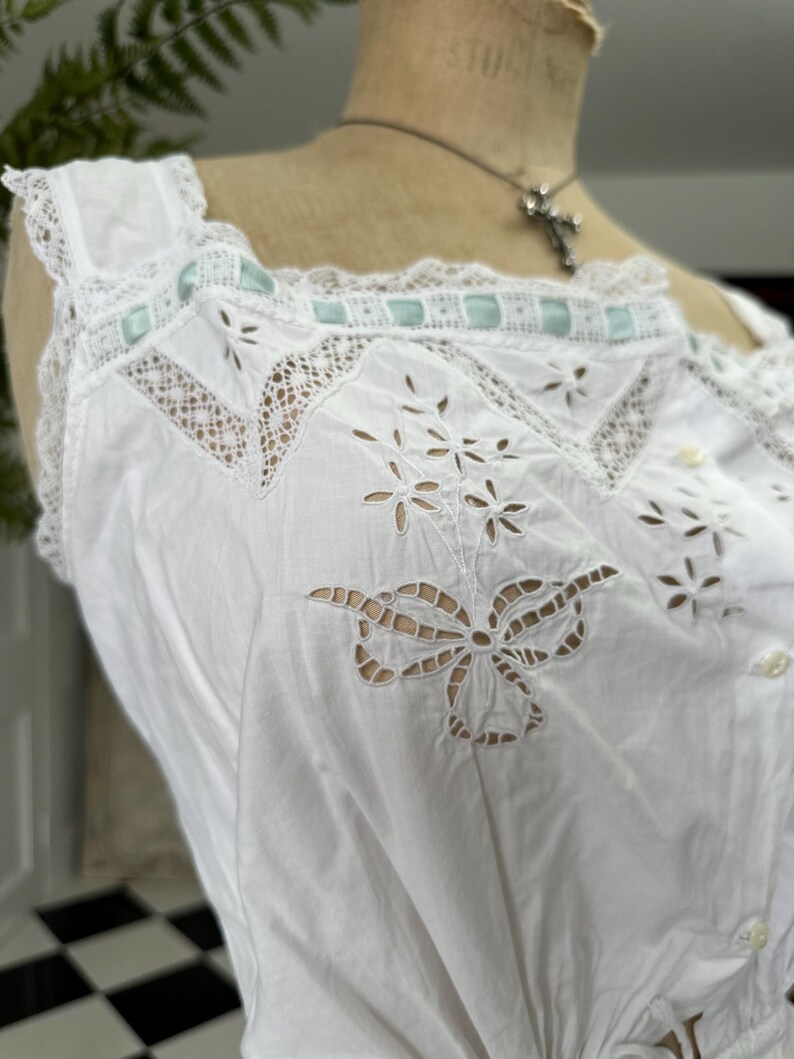 Puede incluir: Top blanco de algod&oacute;n con delicado encaje y dise&ntilde;os de corte intrincados. El top presenta un motivo de mariposa y una fila de botones peque&ntilde;os en la parte delantera.