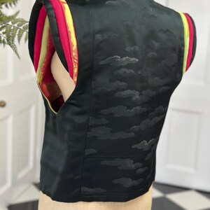 Puede incluir: Chaleco negro sin mangas con un patr&oacute;n de nubes y ribetes amarillos, rojos y verdes en las mangas.