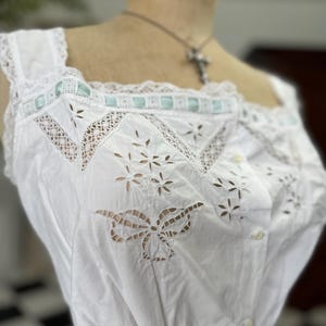 Puede incluir: Camis&oacute;n de algod&oacute;n blanco con encaje de ojal delicado y un ribete de cinta azul claro. El camis&oacute;n tiene cierre de bot&oacute;n y cintura fruncida.