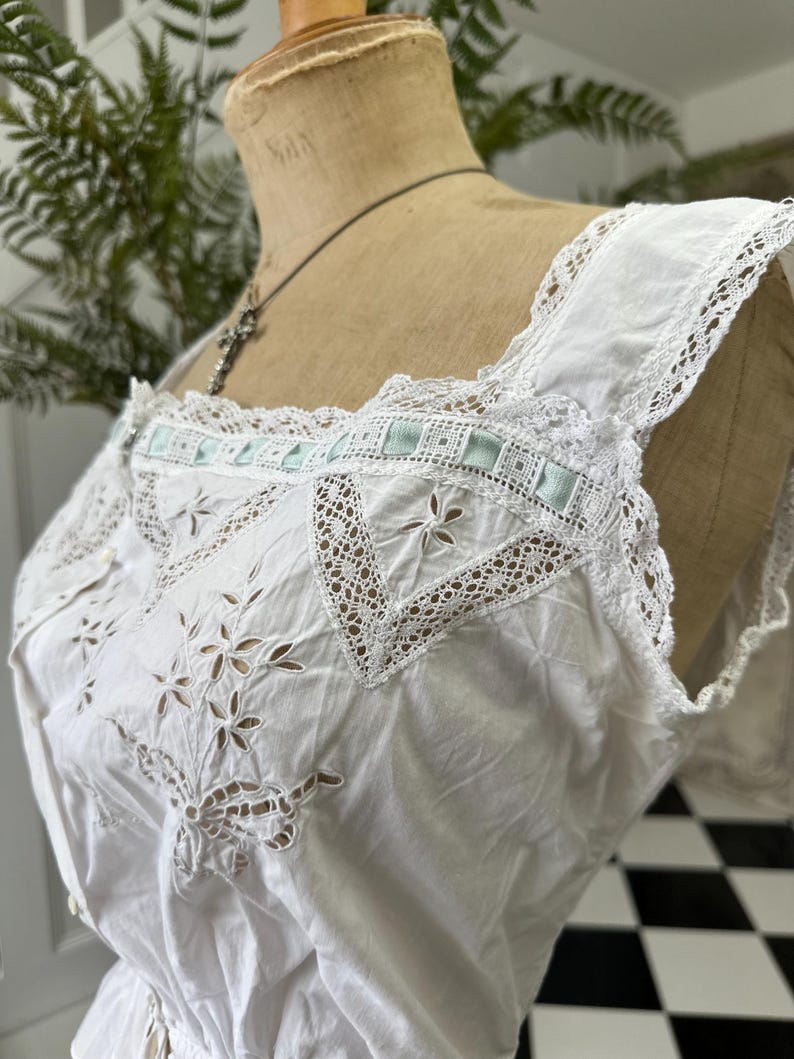 Puede incluir: Top blanco de algod&oacute;n con delicado ribete de encaje y detalles florales bordados. El top presenta un acento de cinta azul claro en el escote.