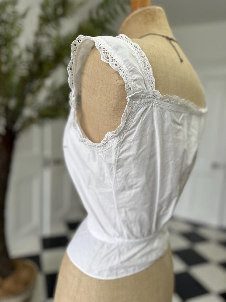 Puede incluir: Camis&oacute;n de algod&oacute;n blanco con ribete de encaje en las tiras y el escote. El camis&oacute;n es ajustado y tiene una cintura fruncida.