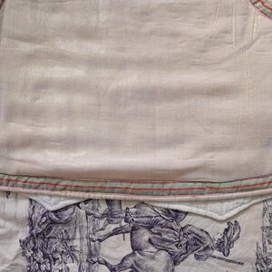 May include: A white fabric with a green and red trim. The fabric has a subtle sheen and is slightly wrinkled. The fabric is lying on a white surface with a floral pattern.