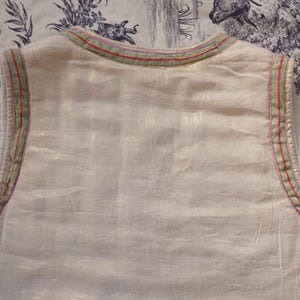 May include: A white sleeveless top with a green and red trim around the neckline. The top is made of a lightweight fabric and has a relaxed fit.