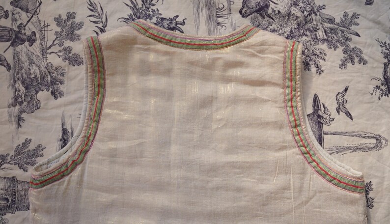 May include: A white sleeveless top with a green and red trim around the neckline. The top is made of a lightweight fabric and has a relaxed fit.