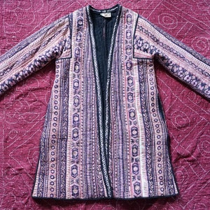 Puede incluir: Una chaqueta larga acolchada con forro negro y un patrón geométrico en tonos de rosa, blanco y azul.