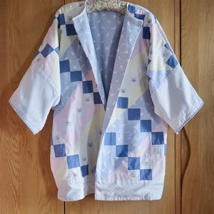 May include: A light blue and pink patchwork kimono with a checkered pattern. The kimono has a long, flowing silhouette and is made of a soft, lightweight fabric.