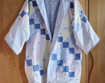 Puede incluir: Un kimono de color azul claro y rosa con un estampado de cuadros. El kimono tiene una silueta larga y fluida y está hecho de una tela suave y ligera.