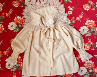 May include: Cream-colored vintage blouse with a large lace collar and cuffs. The blouse features long, puffed sleeves and a satin ribbon tie at the neckline. The fabric has a slightly aged appearance, suggesting its vintage nature. The blouse is buttoned down the front.