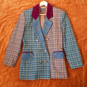 Puede incluir: Una blazer vintage de doble botonadura con un estampado de cuadros en verde azulado, naranja y marrón. La blazer tiene un cuello y ribete de bolsillo de terciopelo burdeos. La etiqueta dice "EASTWEST".